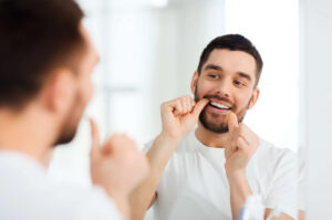 Man in mirror flossing his teeth